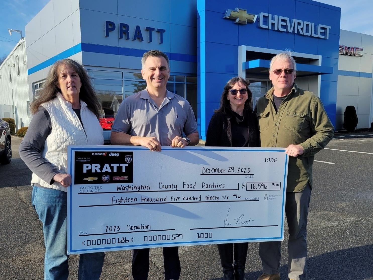 Three individuals proudly display a large check in front of a Chevrolet dealership
