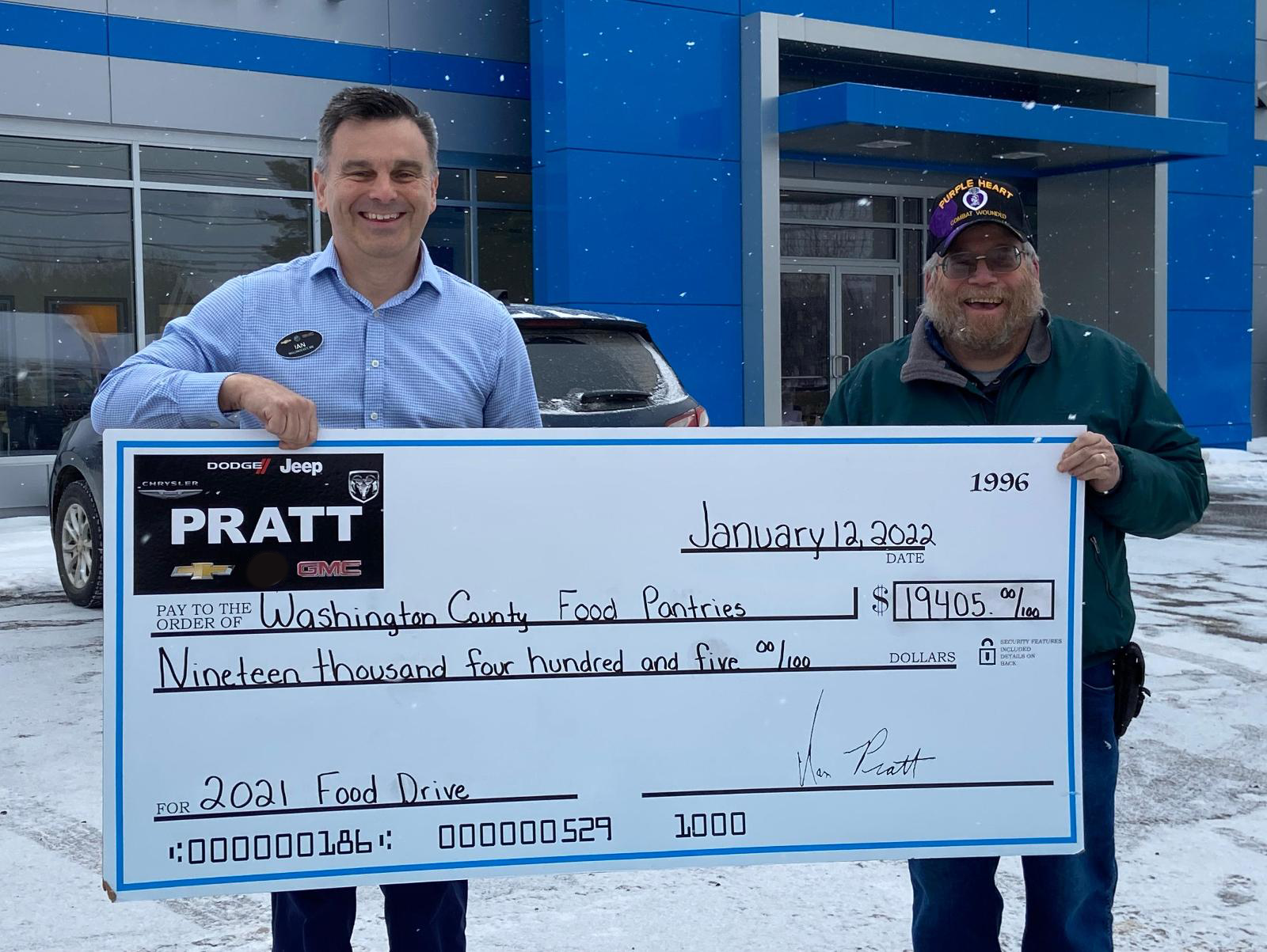 Two individuals proudly display a large check in front of a Chevrolet dealership