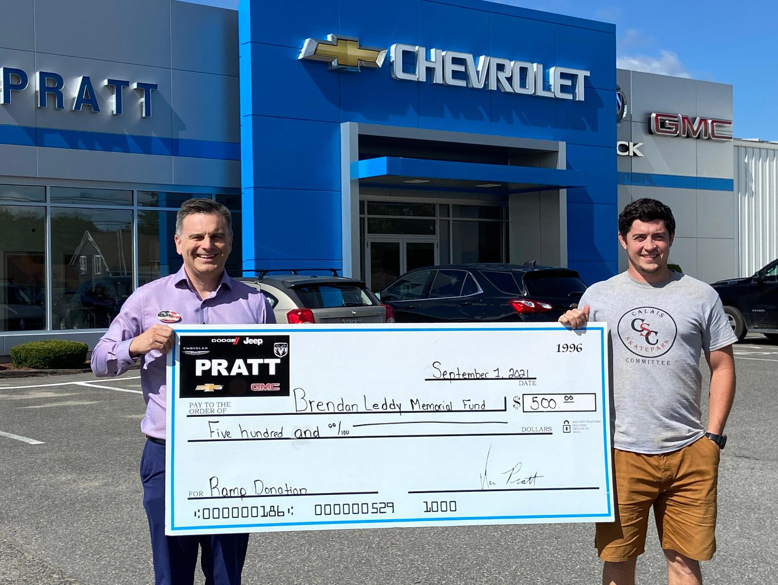 Two individuals proudly display a large check in front of a Chevrolet dealership